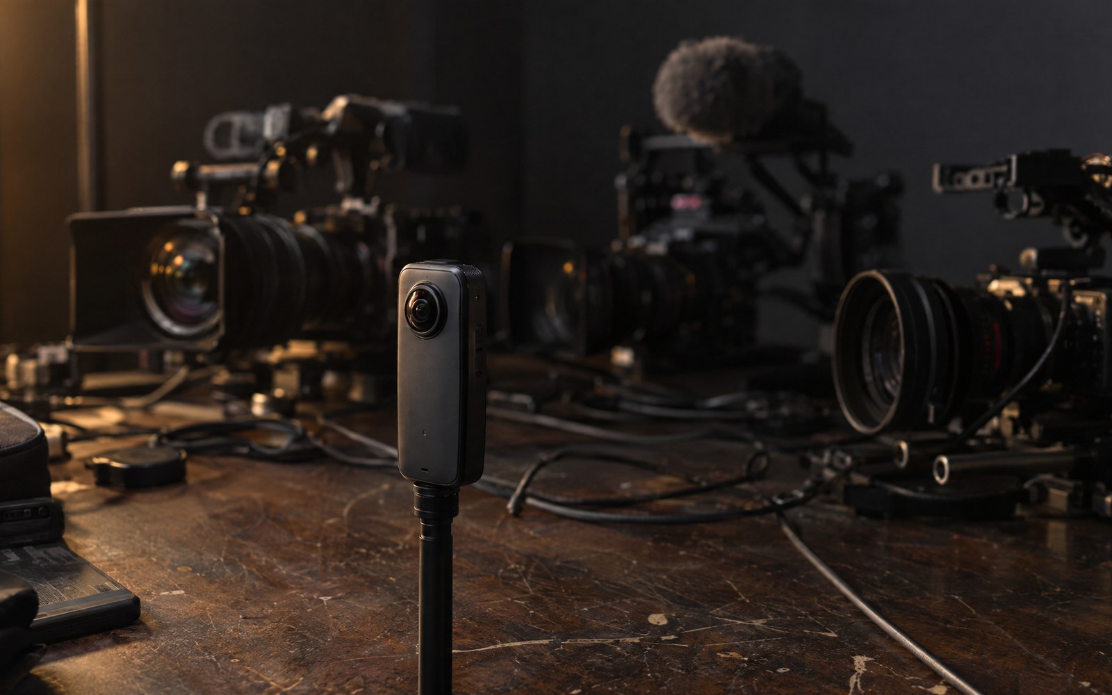 One small 360° camera in front of three large video cameras.